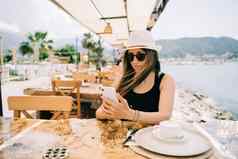 年轻的女孩女夫人太阳镜移动聪明的电话小工具街海边咖啡馆餐厅咖啡商店风景山背景夏天假期假期