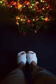 女腿白色毛茸茸的舒适的拖鞋节日圣诞节树晚上光灯黑暗背景前视图