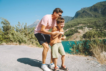 年轻的爸爸儿子站山视图孩子孩子男孩有趣的父亲徒步旅行徒步旅行山湖背景