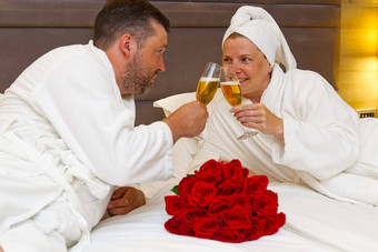 夫妇谎言床上碰杯眼镜香槟庆祝周年纪念日庆祝生日浪漫的日期情人