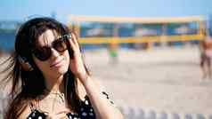 肖像美丽的女孩太阳眼镜穿大黑色的耳机听音乐智能手机海滩热夏天一天背景海滩排球
