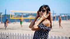 肖像美丽的女孩太阳眼镜穿大黑色的耳机听音乐智能手机海滩热夏天一天背景海滩排球