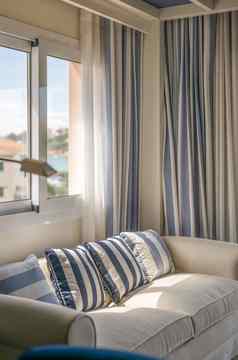 特写镜头舒适的软垫沙发米色颜色装饰枕头垂直blue-beige条纹窗帘风格舒适的生活房间淹没了明亮的阳光窗口