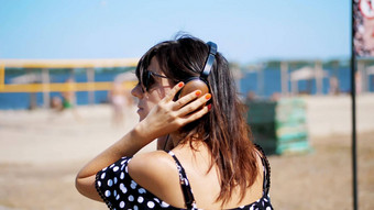 肖像美丽的女孩太阳眼镜穿<strong>大黑</strong>色的耳机听音乐智能手机海滩热夏天一天背景海滩排球