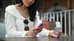 快乐年轻的女人使事务移动银行应用程序坐着在户外咖啡馆