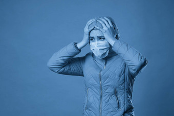 女人穿罩保护脸面具外套蓝色的背景模型女孩医疗面具春天装工作室拍摄复制空间文本抗流感卫生防疫