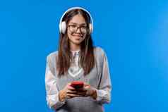 漂亮的亚洲少年听音乐冲浪互联网智能手机女孩微笑快乐蓝色的背景科技成功幸福社会网络概念