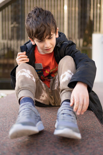 担心年轻的男孩疼痛脸手联合持有腿疼痛脚踝破碎的户外街