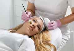 美容师应用粘土面具脸美丽的女人水疗中心治疗脸护理美沙龙