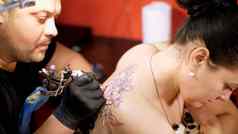 纹身沙龙专家纹身女人的回来花点缀男人。作品特殊的手套特殊的设备画黑色的油漆
