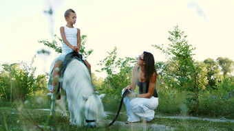 女人男孩走场儿子骑小马妈妈。持有小马缰绳快乐的快乐家庭假期在户外夏天森林
