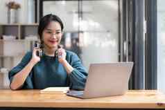 快乐年轻的亚洲种族女经理穿无线耳机移动PC屏幕持有愉快的谈话合作伙伴客户在线工作远程工作场所