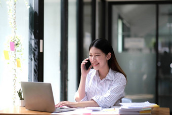 肖像年轻的亚洲业务女人说话智能手机写笔记本移动PC首页办公室美丽的女孩桌子上电脑首页订单启动业务亚洲女人在线锻造电话销售