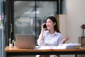 肖像年轻的亚洲业务女人说话智能手机写笔记本移动PC首页办公室美丽的女孩桌子上电脑首页订单启动业务亚洲女人在线锻造电话销售