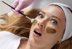美容师应用粘土面具脸美丽的女人水疗中心治疗脸护理美沙龙
