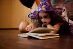 淘气的女孩万圣节化妆穿着女巫女巫向导的他阅读书巫术