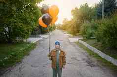 英俊的高加索人十几岁的男孩走街黑色的橙色空气气球庆祝万圣节日落