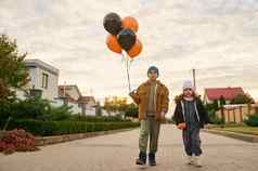 可爱的孩子们男孩女孩哥哥妹妹橙色黑色的气球走国家街万圣节
