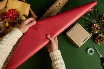 女人的手滚动红色的装饰包装礼物纸绿色背景包装礼物手工艺术