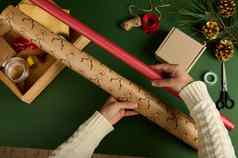 女人的手持有礼物纸选择包装材料包装圣诞节一年礼物绿色背景