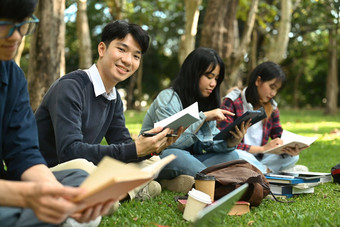 亚洲学生男人。阅读书准备考试绿色草坪上大学校园青年生活方式友谊概念
