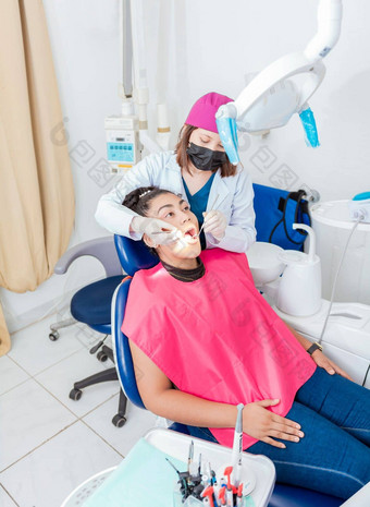 牙医办公室检查女病人的口女牙医检查口青少年女孩说谎椅子女牙医探针牙科镜子检查年轻的女口