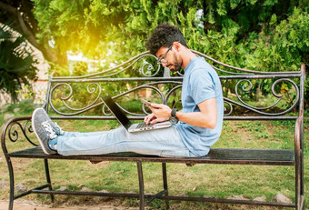 自由职业者男人。坐着公园移动PC手机男人。公园工作在线移动PC放松男人。工作移动PC户外年轻的男人。公园移动PC细胞电话