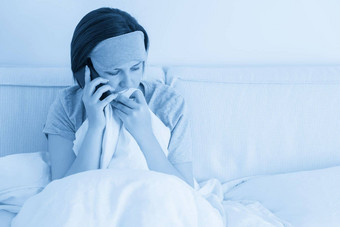 伤心女人穿睡觉面具智能手机坐在床上覆盖羽绒被