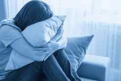 伤心抑郁女人首页坐着沙发上拥抱枕头孤独悲伤概念