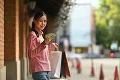 照片满意亚洲女人持有风扇钱色彩斑斓的购物袋站购物区城市
