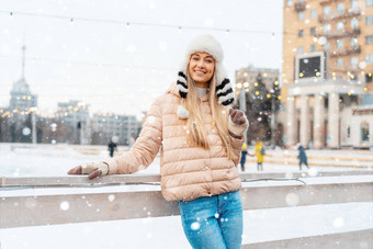 美丽的可爱的中年女孩金发女郎头发温暖的冬天夹克针织手套站冰溜冰场背景小镇广场圣诞节情绪生活方式