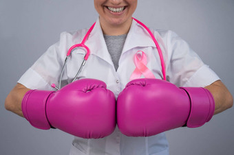 微笑女医生粉红色的拳击手套粉红色的丝带灰色的背景战斗乳房癌症