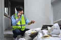 年轻的亚洲男人。检查员会说话的移动电话检查建筑材料建设网站