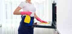 年轻的女人穿手套清洁烤箱厨房清洁服务概念