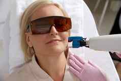 中间岁的女人接收激光治疗美容诊所穿保护眼镜
