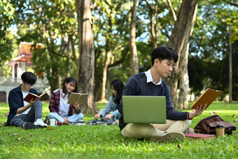 亚洲男人。学生阅读书绿色草坪上大学校园青年生活方式大学友谊概念