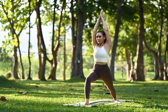 完整的长度运动女人实践瑜伽站战士构成自然环境背景