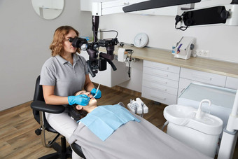 女牙医牙科工具显微镜治疗病人牙齿牙科诊所办公室医学牙科健康护理概念