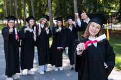 集团快乐学生毕业礼服在户外年轻的女孩文凭手前景