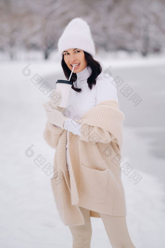 美丽的女孩米色开襟羊毛衫白色他玻璃茶享受雪路堤湖