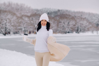 美丽的女孩米色开襟<strong>羊毛</strong>衫白色他玻璃茶享受雪路堤湖