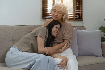 爱的成人女儿拥抱老妈妈。沙发上首页家庭享受温柔的时刻年轻的女人成熟的妈<strong>妈祖</strong>母一代又一代