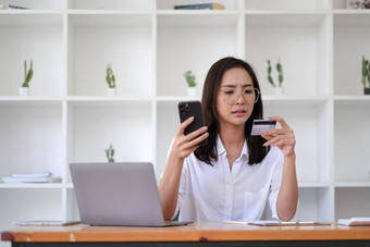 年轻的亚洲女人问题支付伤心女互联网购物者坐沙发上持有电话信<strong>贷</strong>卡感觉抑郁担心痛苦遭受过度<strong>消费</strong>钱卡账户