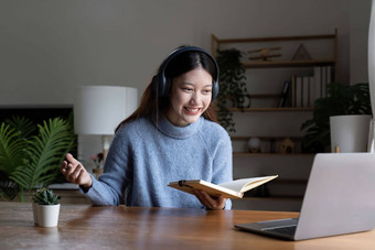 微笑女孩学生穿耳机研究在线老师快乐年轻的亚洲女人学习语言听讲座看网络研讨会写笔记移动PC坐咖啡馆遥远的教育