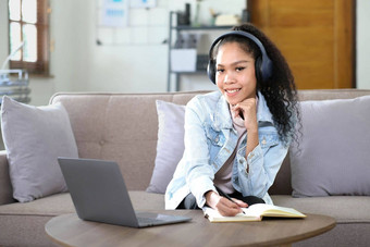 微笑亚洲年轻的女耳机移动PC屏幕听学习在线课程