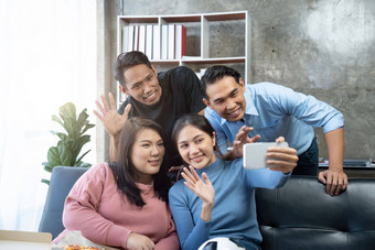 朋友看体育欢呼庆祝快乐多样化的亚洲朋友支持者球迷坐沙发上爆米花饮料视频调用移动电话