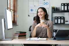 美丽的年轻的亚洲女商人微笑持有咖啡杯子移动PC工作办公室