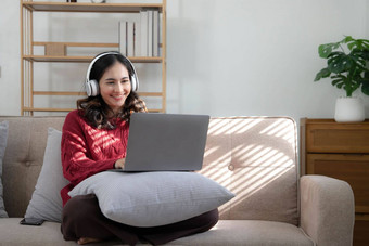 微笑年轻的女人耳机移动PC厅的女研究首页年轻的女人穿耳机听在线网络免费的音频首页