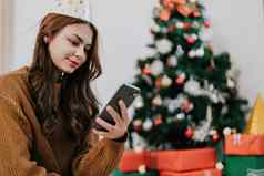 快乐女人阅读打字假期恭喜消息智能手机节日装饰圣诞节树微笑美丽的女聊天移动电话圣诞节云杉积极的情感