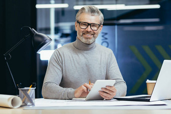 肖像高级架构师灰色的头发的设计师微笑相机男人。模拟计划移动PC平板电脑电脑工作内部工作室办公室